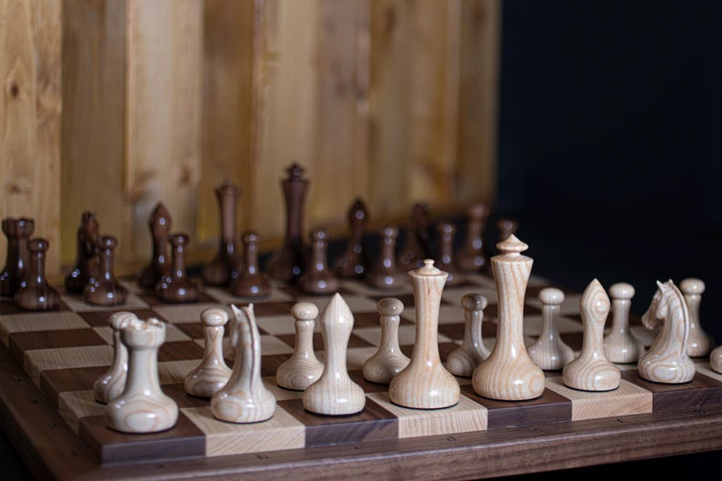 May include: A wooden chess set with light and dark brown pieces on a wooden board with a light and dark brown checkered pattern.