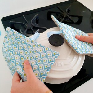 Op de afbeelding: Twee blauwe en groene pottenlapjes met een witte en zwarte deksel op een zwart fornuis. De deksel heeft het woord "SET" erop gedrukt.