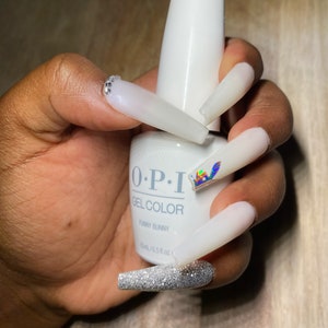 May include: A white bottle of O.P.I. GelColor nail polish with the name "Funny Bunny" printed on the label. The bottle is being held by a hand with long, white, and glittery nails.