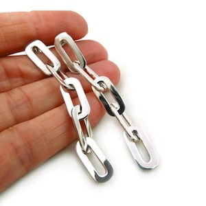 Puede incluir: Pendientes de cadena de plata con un diseño largo y colgante. Los pendientes están hechos de varios eslabones ovalados.