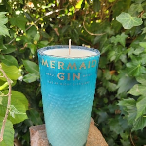 May include: A teal blue glass candle jar with a white wax candle inside. The jar has the text "Mermaid Gin" and "Small Batch Isle of Wight Distillery" printed on it.