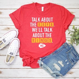 May include: Red t-shirt with white text that reads "Talk about the refs. We'll talk about the rings. KC".
