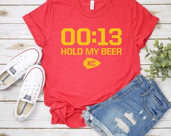 May include: Red t-shirt with the text "00:13 HOLD MY BEER KC" in yellow. The shirt has a distressed look and is made of a soft, comfortable material.