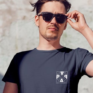 Könnte beinhalten: Marineblaues T-Shirt mit weißem quadratischem Grafikdesign auf der Brust. Das Design enthält die Buchstaben "P", "A" und "Q". Das kurzärmlige T-Shirt wird von einer Person mit Sonnenbrille getragen.