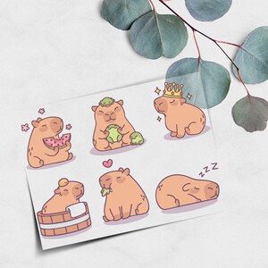 Könnte beinhalten: Ein Bogen mit Aufklebern mit Cartoon-Wasserschweinen in verschiedenen Posen. Eines isst Wassermelone, ein anderes hat einen Frosch auf dem Kopf und ein weiteres trägt eine Krone. Die Aufkleber sind pfirsichfarben mit schwarzen Umrissen.