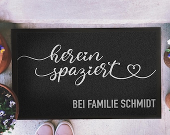 May include: Black welcome mat with white text that says "herein spaziert" with a heart symbol and "BEI FAMILIE SCHMIDT" at the bottom.