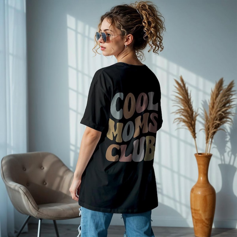 May include: Black t-shirt with a graphic print on the back that says "Cool Moms Club" in colorful, retro-style lettering.