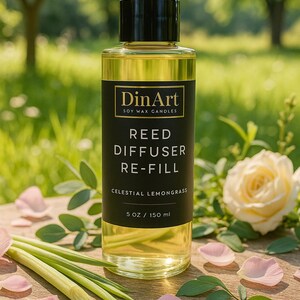 Pode incluir: Uma garrafa de vidro transparente de recarga de difusor de palheta de vela de cera de soja DinArt com aroma Celestial Lemongrass. A garrafa tem um r&oacute;tulo preto com texto branco e uma tampa preta. Cont&eacute;m 150 ml de l&iacute;quido. A imagem inclui uma rosa e capim-lim&atilde;o.
