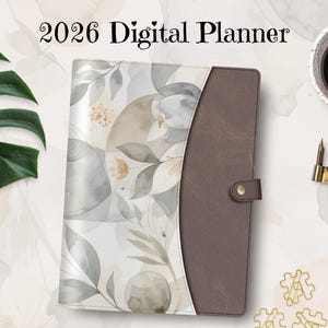 Peut inclure: Un agenda numérique avec le texte "2026 Digital Planner". L'agenda présente une couverture en cuir marron avec une fermeture à bouton et un motif floral aux tons neutres. Une tasse de café et un stylo sont également visibles.