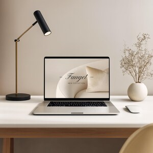May include: A modern desk setup featuring a laptop displaying the "Fauget New Collection" logo. A black and gold desk lamp illuminates the scene, alongside a white mouse and a vase with dried flowers. The desk is white.