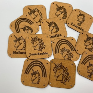 Puede incluir: Una colección de 10 etiquetas cuadradas de madera marrón con un diseño de unicornio y arcoíris. Cada etiqueta tiene un nombre diferente, incluyendo Lena-Sophie, Leonie, Emilia y Helena.