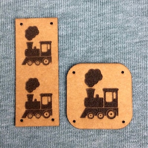 Puede incluir: Dos etiquetas de madera marrón con una silueta negra de una locomotora en cada una. Las etiquetas son rectangulares y tienen esquinas redondeadas. La locomotora tiene una chimenea y ruedas.