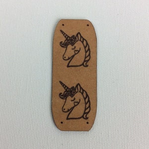 Könnte beinhalten: Ein braunes Leder-Etikett mit zwei Designs von Pferdeköpfen. Die Pferdeköpfe sind schwarz und weiß und haben geschlossene Augen.