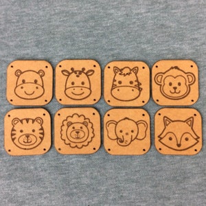 Könnte beinhalten: Acht Holzkacheln mit verschiedenen Tiergesichtern, die darauf graviert sind. Die Tiere sind ein Flusspferd, eine Giraffe, ein Zebra, ein Affe, ein Tiger, ein Löwe, ein Elefant und ein Fuchs.