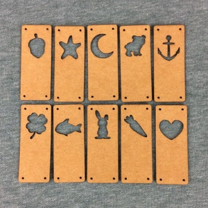 May include: Ten wooden tags with various shapes cut out, including an acorn, a star, a crescent moon, a bear, an anchor, a clover, a fish, a rabbit, a carrot, and a heart. The tags are all brown and have a rough texture.