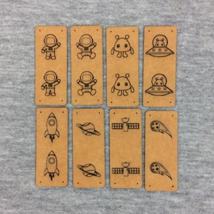 Könnte beinhalten: Acht braune rechteckige Etiketten mit verschiedenen Weltraum-Illustrationen. Die Illustrationen zeigen Astronauten, Außerirdische, Raumschiffe, Planeten und Kometen.