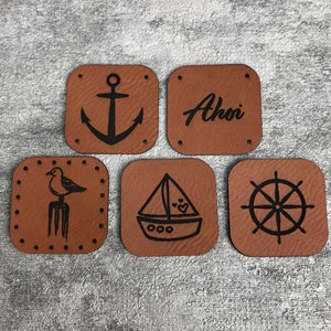May include: Five brown leather patches with nautical designs. The patches feature an anchor, a sailboat, a seagull, a ship's wheel, and the word "Ahoy!"
