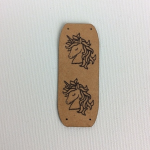 Könnte beinhalten: Ein braunes Leder-Etikett mit zwei Einhorn-Designs. Das Etikett hat zwei Löcher oben zum Anbringen.