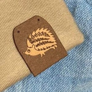 Puede incluir: Dos parches de cuero marrón con un diseño de erizo cosidos en una tela vaquera azul claro.