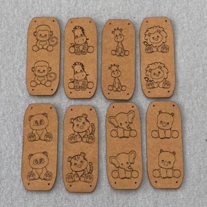 Puede incluir: Doce etiquetas de madera marrón con diferentes diseños de animales, incluyendo un mono, una cebra, una jirafa, un león, un panda, un tigre, un elefante y un hipopótamo.