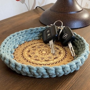 Könnte beinhalten: Eine tealblaue gehäkelte Schale mit einem Holzsockel, der mit einem Mandala-Muster verziert ist. Zwei Autoschlüssel liegen in der Schale.