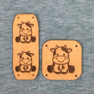 May include: Two wooden cow appliques, one rectangular and one long and narrow, with a brown background and black cow designs.