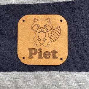 Puede incluir: Una etiqueta de madera marrón con un dibujo de línea negra de un mapache y el nombre "Piet" escrito en negro.