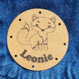 May include: A brown leather patch with a fox illustration and the name Leonie in a circle.