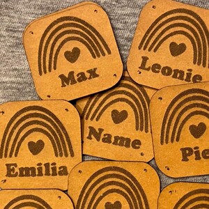 Puede incluir: Siete parches de cuero marrón con diseños de arcoíris y corazón. Cada parche tiene un nombre diferente impreso: Max, Leonie, Name, Piet, Emilia, Emma y Lukas.