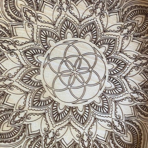 May include: A wooden mandala with a brown geometric design in the center. The mandala is surrounded by a intricate pattern of leaves and swirls.