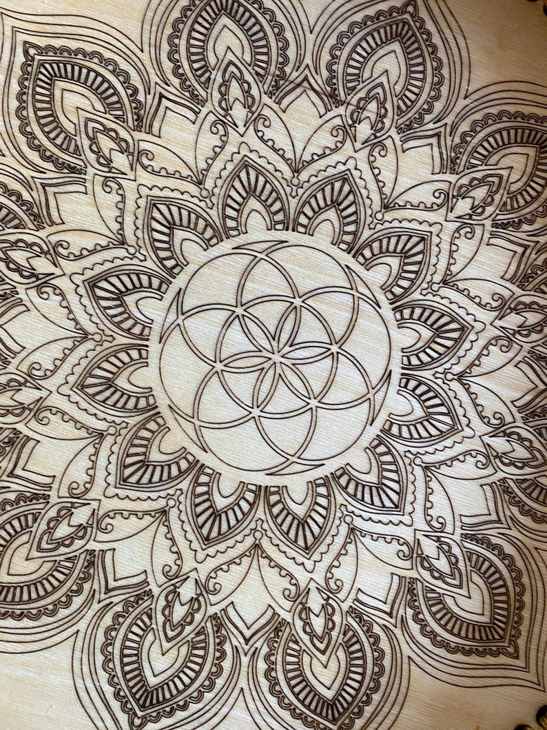 May include: A wooden mandala with a brown geometric design in the center. The mandala is surrounded by a intricate pattern of leaves and swirls.