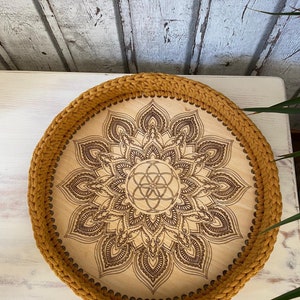 May include: A round wooden tray with a brown mandala design and a mustard yellow crocheted border.
