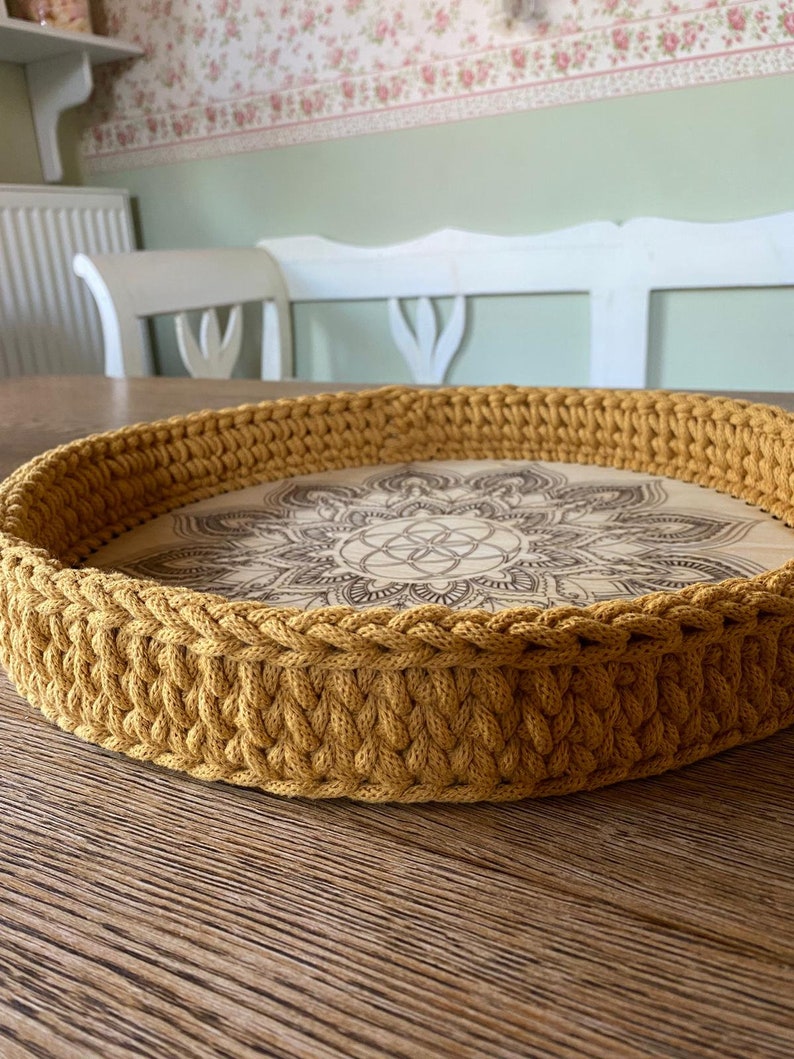 May include: A round, mustard yellow crocheted tray with a wooden base featuring a mandala design.