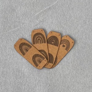 Puede incluir: Cinco etiquetas de papel marrón con diseños de arcoíris. Cada etiqueta tiene un diseño de arcoíris diferente con un corazón o una estrella.