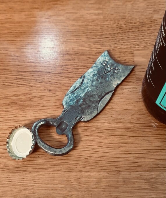 A hand-forged metal owl that actually opens your beer — tiny blacksmith sculpture meets totally functional BBQ sidekick.