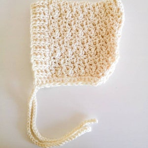 May include: A crocheted baby bonnet in a cream colour with a long tie.