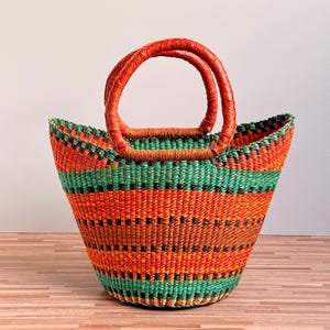 May include: A handwoven basket featuring a vibrant pattern of horizontal stripes in bright orange, emerald green, and black. The basket has a wide, open top and two sturdy, rounded handles wrapped in a matching orange material for carrying.