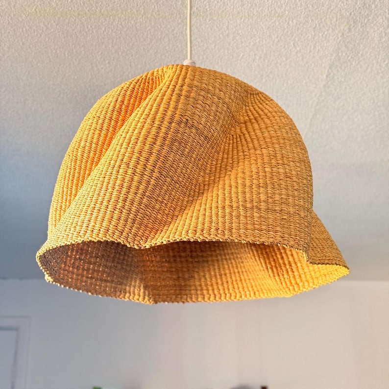 K&ouml;nnte beinhalten: Gelb-goldene H&auml;ngeleuchte aus geflochtenem Material. Der Lampenschirm hat eine einzigartige, ausgestellte Form und eine strukturierte, korbartige Optik. Die Leuchte wird an einem wei&szlig;en Kabel aufgeh&auml;ngt. Durchmesser ca. 40 cm.