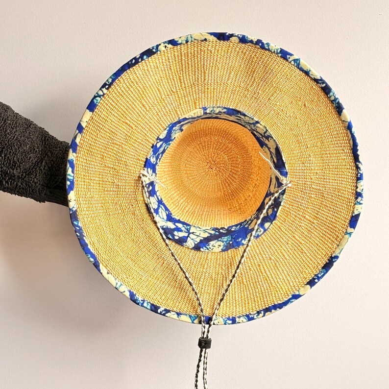 Puede incluir: Un sombrero de paja de ala ancha con una textura tejida en tono bronceado natural. El sombrero est&aacute; acentuado con un borde de tela con estampado azul y blanco a lo largo del borde exterior y la corona interior. Incluye una correa ajustable.