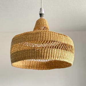 K&ouml;nnte beinhalten: Eine H&auml;ngeleuchte aus geflochtenem Rattan. Die Leuchte hat einen breiten, abgerundeten Schirm mit offenem Webmuster. Der Schirm hat eine nat&uuml;rliche, beige Farbe und h&auml;ngt an einem wei&szlig;en Kabel. Durchmesser ca. 40 cm.