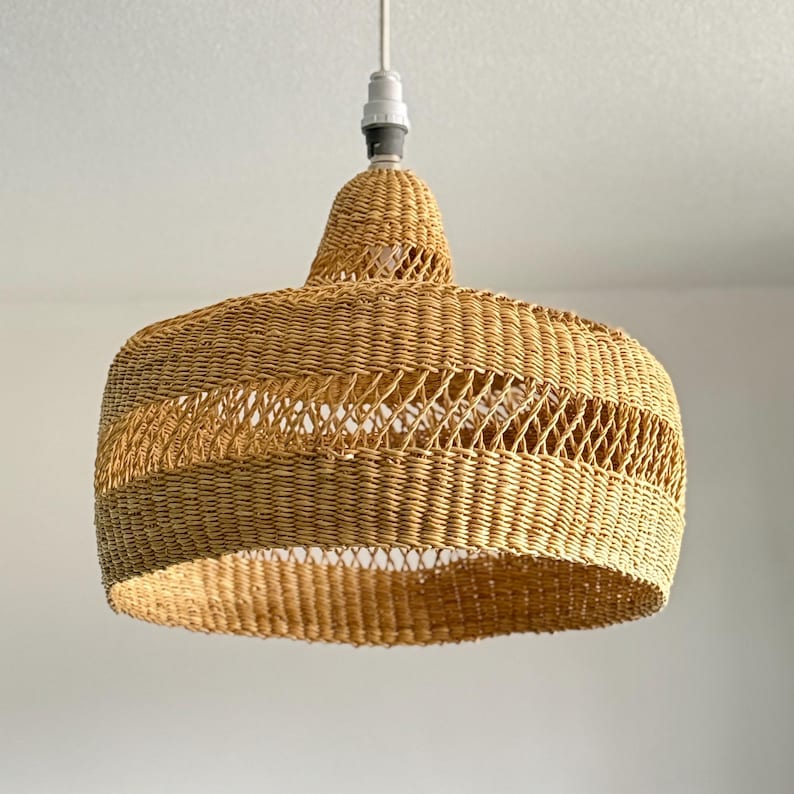 K&ouml;nnte beinhalten: Eine H&auml;ngeleuchte aus geflochtenem Rattan. Die Leuchte hat einen breiten, abgerundeten Schirm mit offenem Webmuster. Der Schirm hat eine nat&uuml;rliche, beige Farbe und h&auml;ngt an einem wei&szlig;en Kabel. Durchmesser ca. 40 cm.
