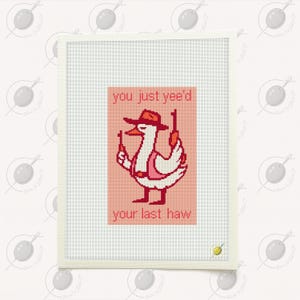 以下が含まれることがあります： カウボーイハットとベストを着て2丁の銃を持っている白いガチョウを描いたクロスステッチアート。テキストは赤で「you just yee'd your last haw」と書かれています。アートワークは白いフレームに入っています。