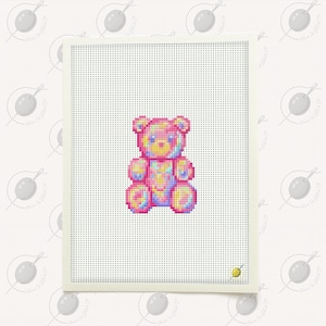 May include: A cross-stitch design of a teddy bear in shades of pink, yellow, and blue. The bear is centered on a white perforated canvas, framed by a cream-colored border. The background features a repeating pattern of a needle and thread.