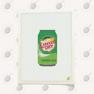 Puede incluir: Un punto de cruz de una lata verde de Canada Dry ginger ale. La lata presenta el logotipo de la marca en rojo y amarillo, con las palabras "GINGER ALE" debajo. La obra de arte está enmarcada en blanco.