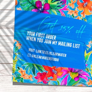 May include: A vibrant watercolor design featuring tropical flowers in shades of pink, orange, and green. A blue banner displays the text "Get 15% off" and information about joining a mailing list. The background is a light wood surface.