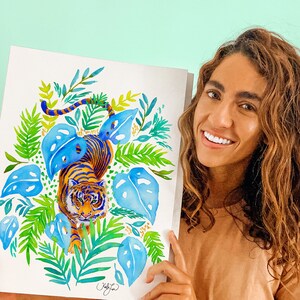 Puede incluir: Una pintura de acuarela de un tigre caminando por una escena de jungla. El tigre es naranja y negro con follaje azul y verde que lo rodea. La pintura est&aacute; firmada "Kelly" en la esquina inferior derecha.