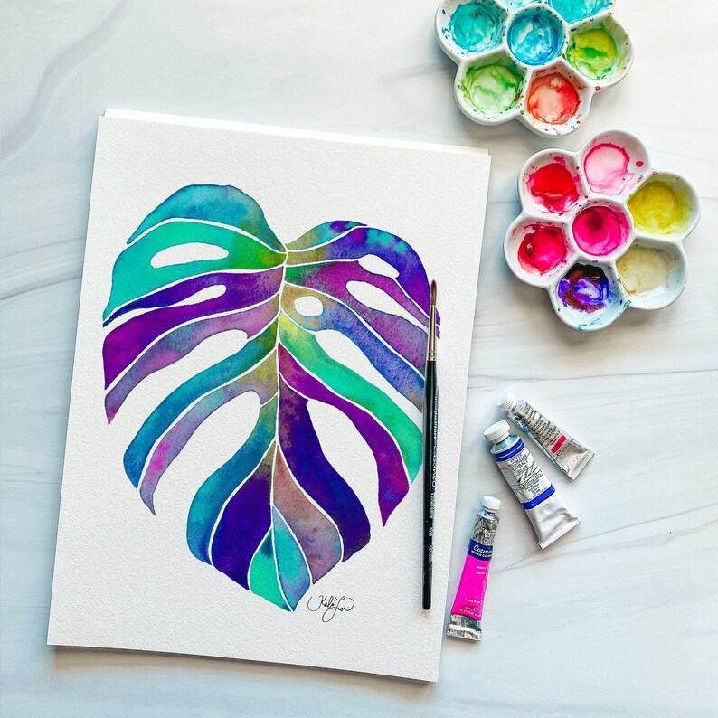 May include: A watercolor painting of a large, vibrant monstera leaf with shades of purple, blue, and green. The leaf is painted on a white background and is surrounded by paint palettes and paint tubes.