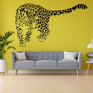 May include: A black silhouette of a leopard walking on a yellow wall. The leopard is facing the left side of the image. The wall is behind a gray couch with white pillows.
