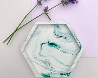 May include: A hexagonal tray with a white and green marbled design. The tray is made of concrete and has a smooth, polished finish.