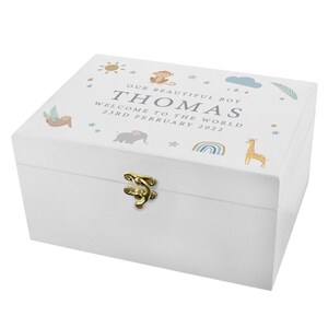 May include: White wooden keepsake box with a gold-colored clasp. The lid features the text "OUR BEAUTIFUL BOY THOMAS WELCOME TO THE WORLD 23RD FEBRUARY 2022" and illustrations of a sun, monkey, cloud, sloth, elephant, rainbow, giraffe, and stars.
